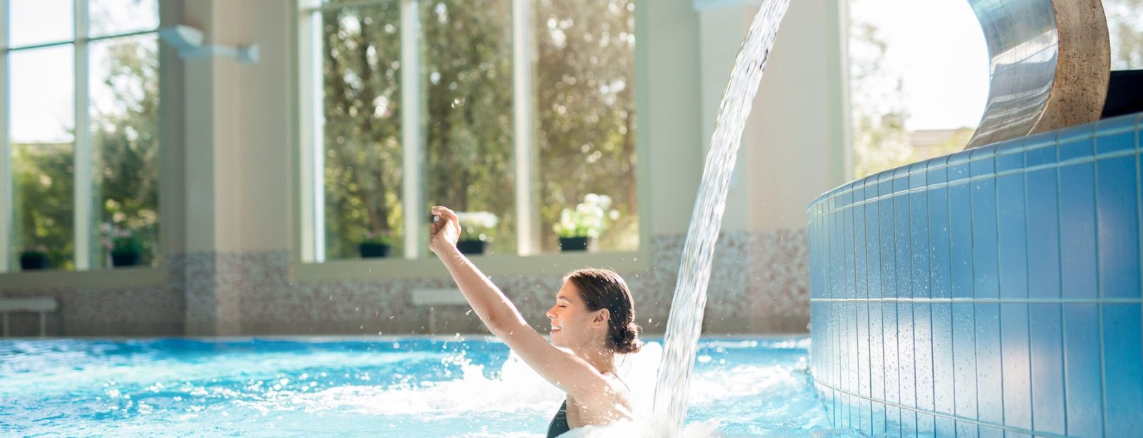 Young happy woman enjoying warm waterfall in spa jacuzzi